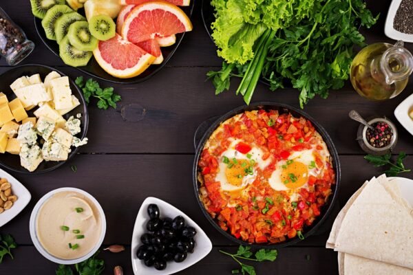 A plate with feta cheese, olives, tomatoes, cucumbers, whole-grain bread, and a boiled egg, served with Turkish coffee on a rustic wooden table.