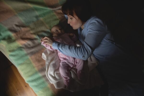 Mother comforting a crying newborn in a dark bedroom, looking tired and unsure what to do next.