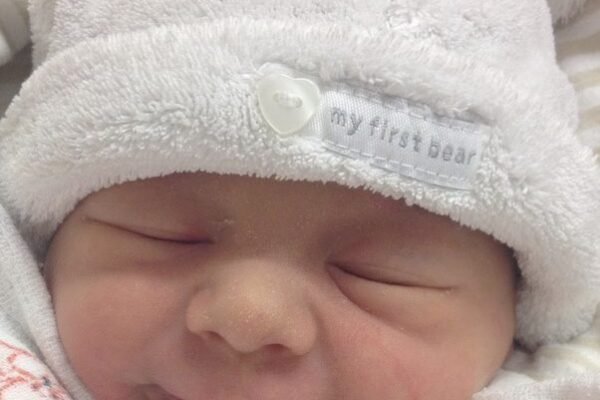 Newborn baby in soft white bear hat showing reflex smile with eyes closed