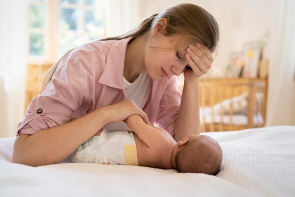 Newborn baby crying after bottle feed, held by tired mother in dimly lit room